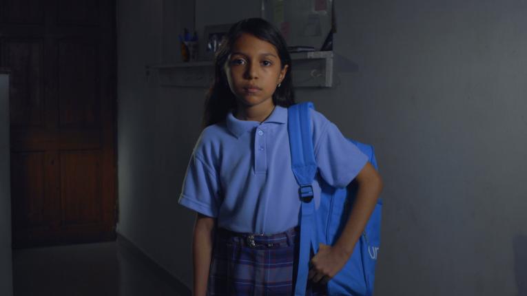 Niña en uniforme con mochila en un hombro.
